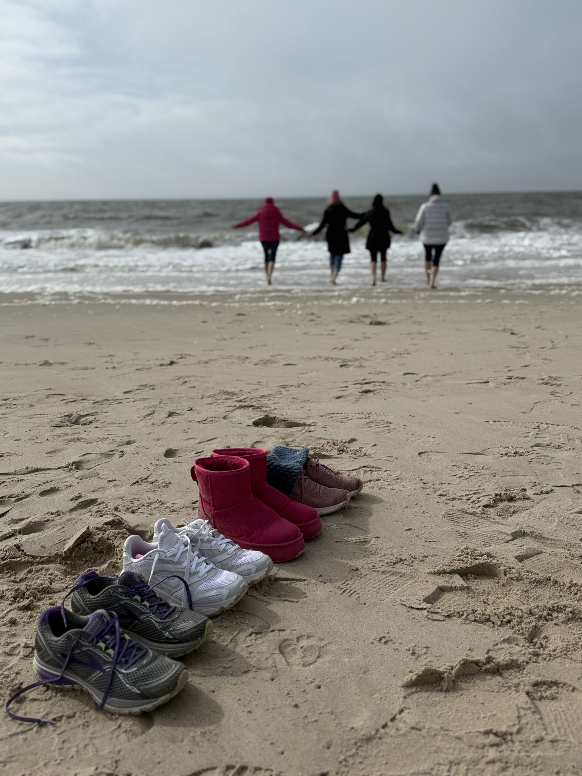 Schuhe im Sand, vier Frauen laufen Hand in Hand ins Meer